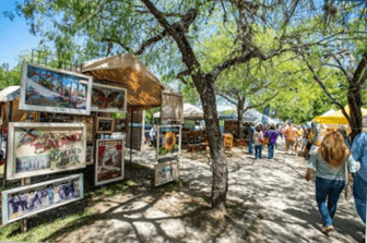 A sunny outdoor market scene with tents, artwork displays, and people strolling along a path.