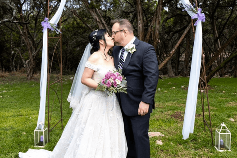 A bride and groom share a kiss during their outdoor wedding ceremony.