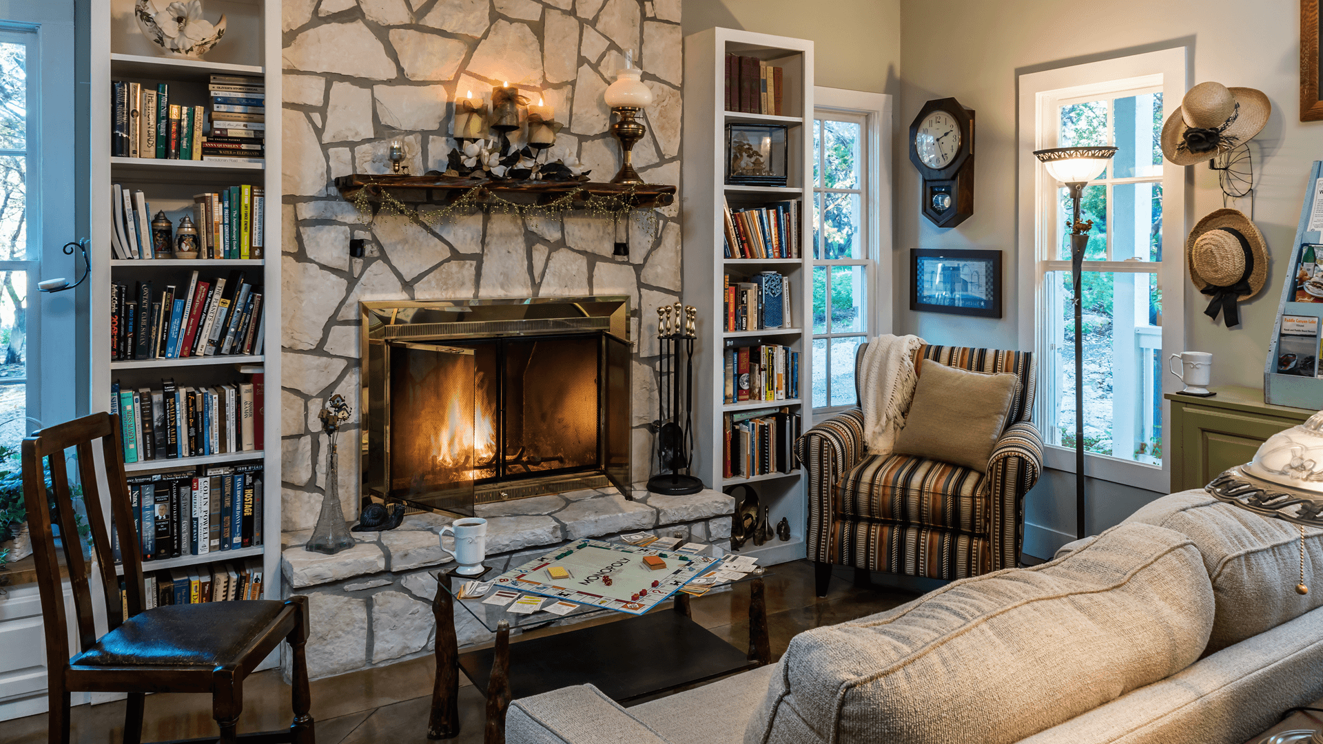 A cozy living room featuring a stone fireplace, bookshelves, and a game of Monopoly on the coffee table.