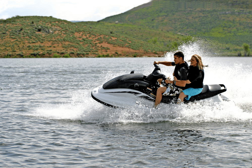 A man and a woman enjoy riding a jet ski on a lake, creating splashes in the water.