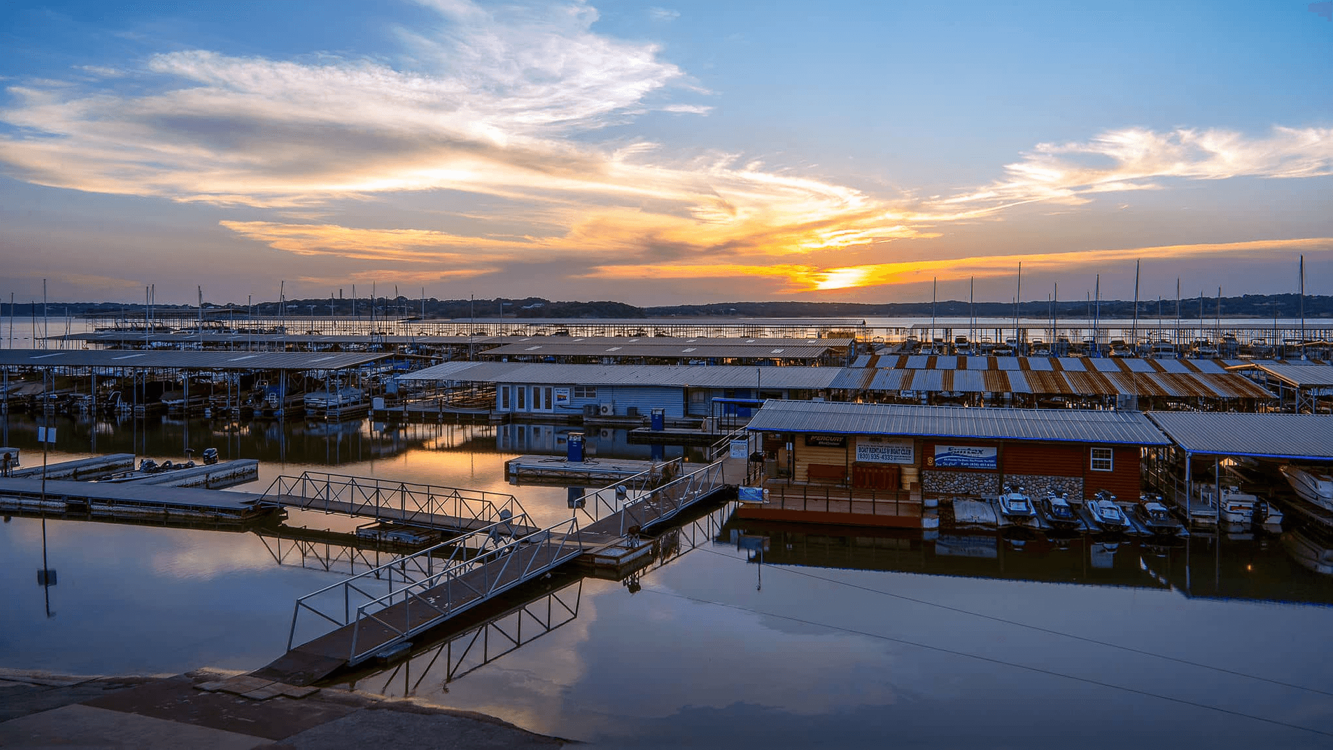 Sunset over a calm marina with boats and reflections in the water.