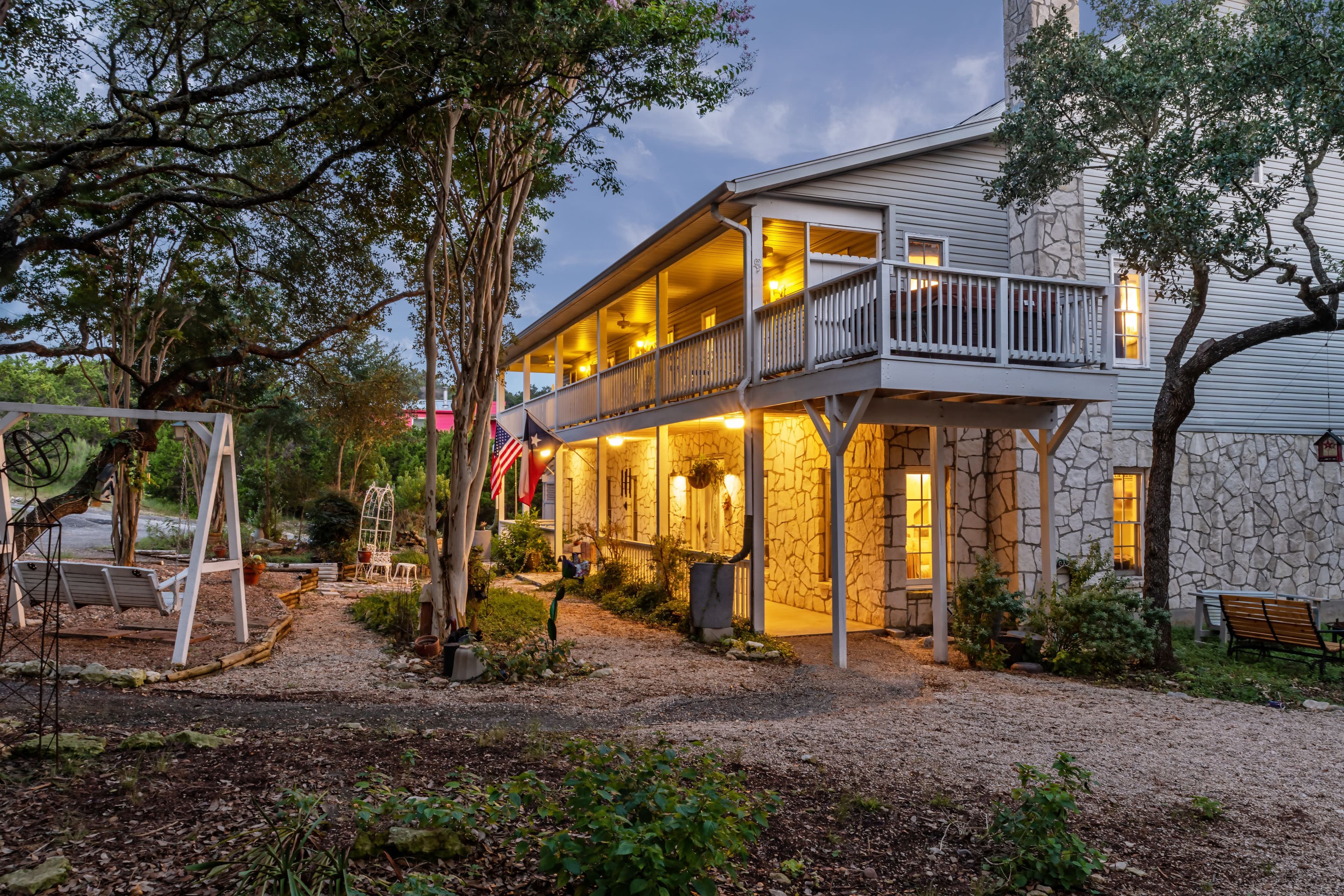 A charming two-story house illuminated at dusk, surrounded by lush greenery and a gravel pathway. A charming two-story house illuminated at dusk, surrounded by lush greenery and a gravel pathway.