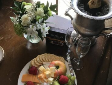 photo of bottle of champaign, a fruit and cheese plate and lovely roses
