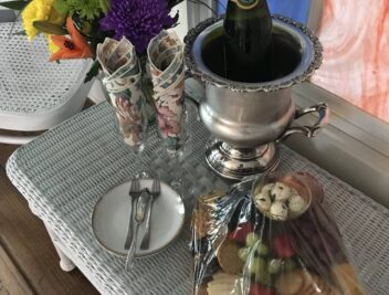 photo of bottle of champaign, seasonal flowers and a fruit and cheese platter